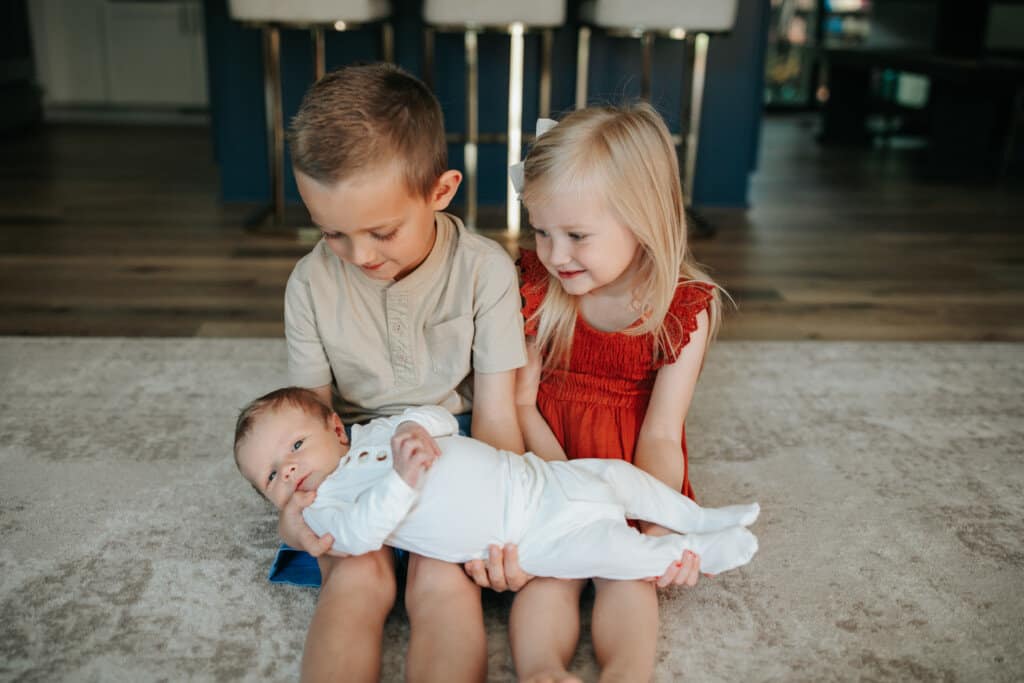 two older siblings (a boy and a girl) holding their new baby brother